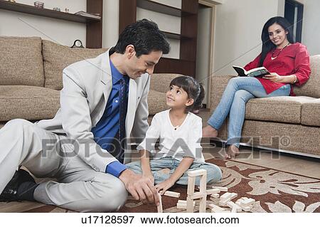 Stock Photo - Woman looking at her daughter playing Jenga with her father. Fotosearch