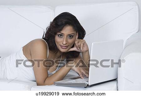 Stock Photo - Woman lying on a couch and using a laptop. Fotosearch
