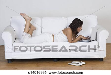 Woman lying on a couch and using a laptop View Large Photo Image Stock Photography - Woman lying on a couch and using a laptop. Fotosearch