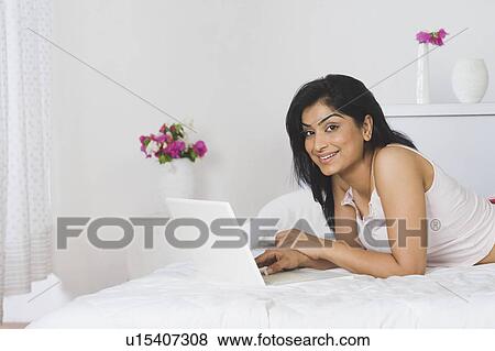 Woman lying on the bed and using a laptop View Large Photo Image Stock Photo - Woman lying on the bed and using a laptop. Fotosearch