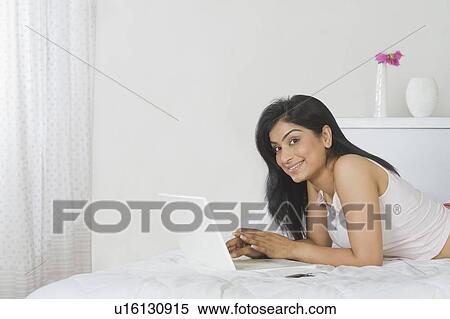 Stock Photography - Woman lying on the bed and using a laptop. Fotosearch