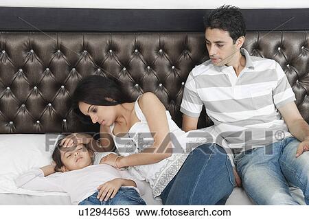 Stock Image - Woman making her daughter sleep with her husband beside her. Fotosearch