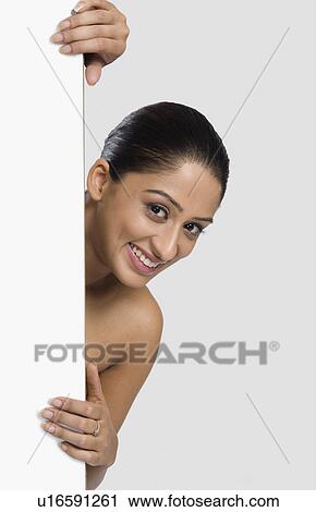Stock Image - Woman peeking from behind a door. Fotosearch
