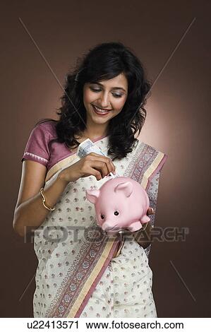 Stock Image - Woman putting a currency note into a piggy bank. Fotosearch