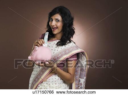 Woman putting a currency note into a piggy bank View Large Photo Image Stock Photograph - Woman putting a currency note into a piggy bank. Fotosearch