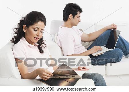 Stock Image - Woman reading a magazine with a man using a laptop. Fotosearch