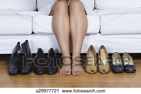 Stock Image - Woman sitting on a couch and choosing footwear. Fotosearch