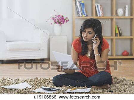 Woman sorting out bills while talking on a mobile phone View Large Photo Image Stock Photograph - Woman sorting out bills while talking on a mobile phone. Fotosearch