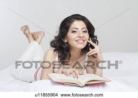 Picture - Woman talking holding a book and talking on a mobile phone on the bed. Fotosearch