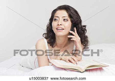 Woman talking holding a book and talking on a mobile phone on the bed View Large Photo Image Stock Photo - Woman talking holding a book and talking on a mobile phone on the bed. Fotosearch