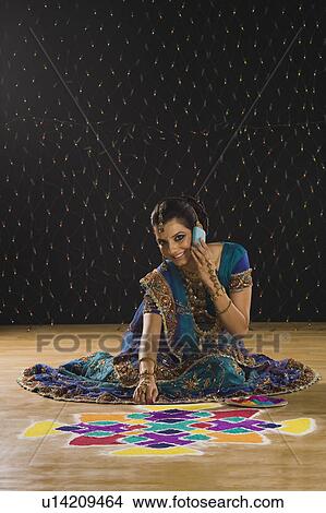 Picture - Woman talking on a mobile phone and making rangoli. Fotosearch