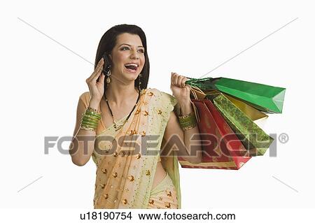 Picture - Woman talking on a mobile phone and holding shopping bags. Fotosearch
