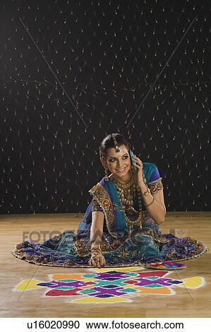 Stock Image - Woman talking on a mobile phone and making rangoli. Fotosearch