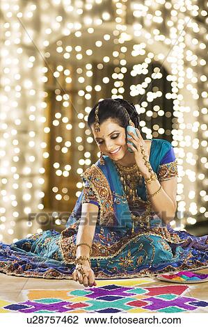 Stock Image - Woman talking on a mobile phone and making rangoli. Fotosearch