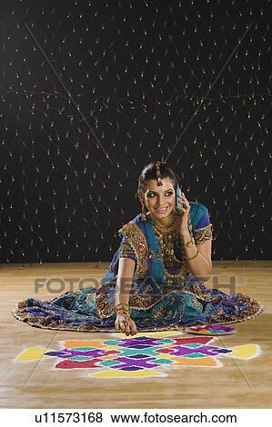 Stock Photo - Woman talking on a mobile phone and making rangoli. Fotosearch