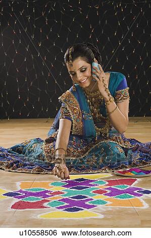 Stock Photograph - Woman talking on a mobile phone and making rangoli. Fotosearch