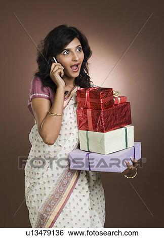 Stock Photograph - Woman talking on a mobile phone and holding gifts. Fotosearch