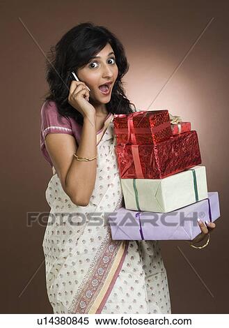 Stock Photography - Woman talking on a mobile phone and holding gifts. Fotosearch