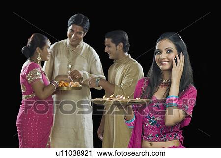 Stock Image - Woman talking on a mobile phone with her family in the background. Fotosearch