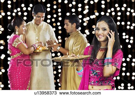 Woman talking on a mobile phone with her family in the background View Large Photo Image Stock Image - Woman talking on a mobile phone with her family in the background. Fotosearch