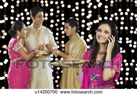 Woman talking on a mobile phone with her family in the background View Large Photo Image Stock Image - Woman talking on a mobile phone with her family in the background. Fotosearch