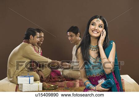 Woman talking on a mobile phone with her family in the background View Large Photo Image Stock Image - Woman talking on a mobile phone with her family in the background. Fotosearch