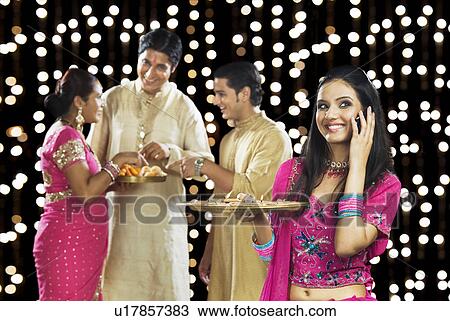 Woman talking on a mobile phone with her family in the background View Large Photo Image Stock Image - Woman talking on a mobile phone with her family in the background. Fotosearch