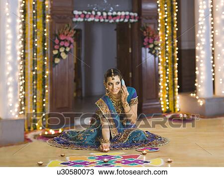 Stock Image - Woman talking on a mobile phone with decorating oil lamps near rangoli. Fotosearch
