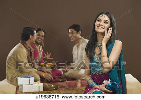 Woman talking on a mobile phone with her family in the background View Large Photo Image Stock Photograph - Woman talking on a mobile phone with her family in the background. Fotosearch
