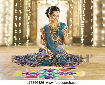 Stock Photograph - Woman text messaging on a mobile phone near rangoli. Fotosearch