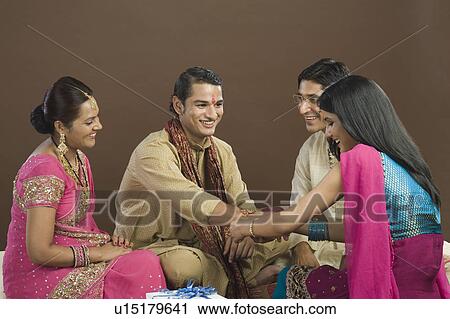 Stock Image - Woman tying rakhi on the wrist of her brother. Fotosearch