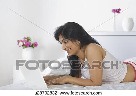 Stock Image - Woman using a laptop on the bed. Fotosearch