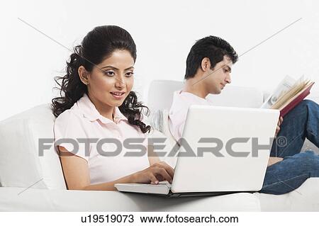 Woman using a laptop with her boyfriend reading a book View Large Photo Image Stock Image - Woman using a laptop with her boyfriend reading a book. Fotosearch