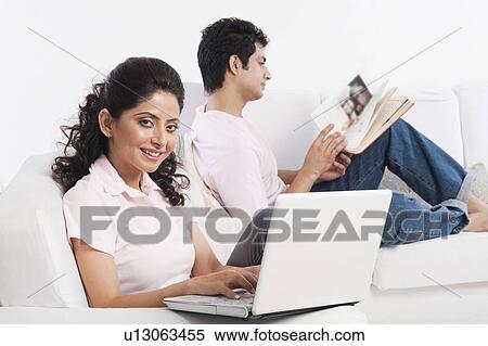 Woman using a laptop with her boyfriend reading a book View Large Photo Image Stock Photography - Woman using a laptop with her boyfriend reading a book. Fotosearch