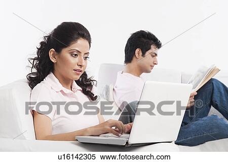 Woman using a laptop with her boyfriend reading a book View Large Photo Image Stock Photography - Woman using a laptop with her boyfriend reading a book. Fotosearch