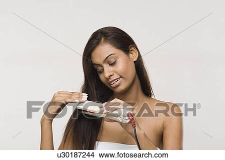 Picture - Woman using straightening irons on her hair. Fotosearch