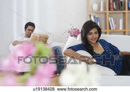 Stock Photo - Woman watching television while her husband reading newspaper in the background. Fotosearch