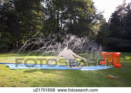 Boy playing in sprinkler in backyard View Large Photo Image Stock Photo - Boy playing in sprinkler in backyard. Fotosearch