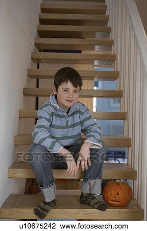 Stock Image - Boy sitting on steps with carved pumpkin. Fotosearch