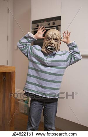 Stock Image - Boy wearing Halloween mask in kitchen. Fotosearch