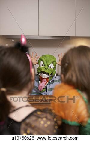 Stock Photograph - Boy wearing Halloween mask in kitchen. Fotosearch