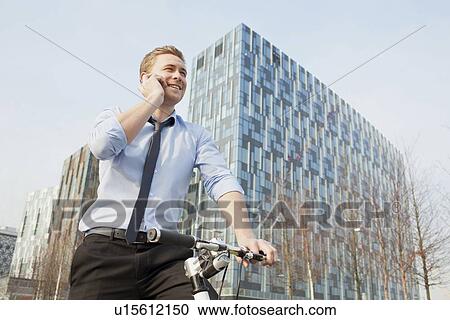 Stock Image - Businessman riding bicycle outdoors. Fotosearch
