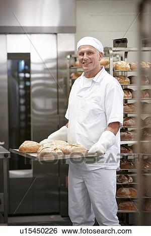Stock Photograph - Chef carrying tray of bread in kitchen. Fotosearch