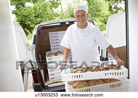 Stock Image - Chef carrying trays of bread to van. Fotosearch