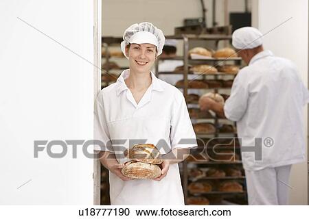 Stock Image - Chef holding loaves of bread in kitchen. Fotosearch