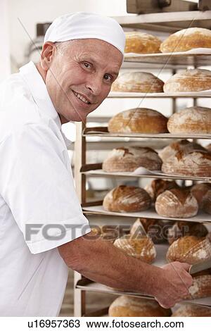 Stock Image - Chef putting tray of bread on rack. Fotosearch