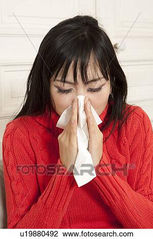 Stock Image - Close up of woman blowing her nose. Fotosearch