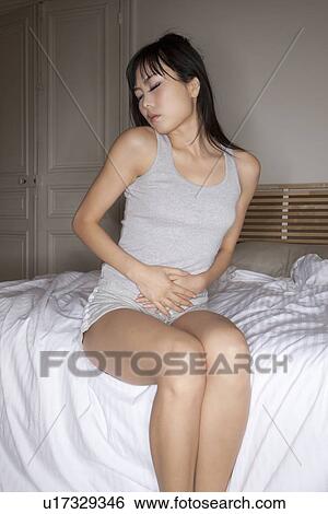 Frowning woman holding belly on bed View Large Photo Image Stock Photograph - Frowning woman holding belly on bed. Fotosearch