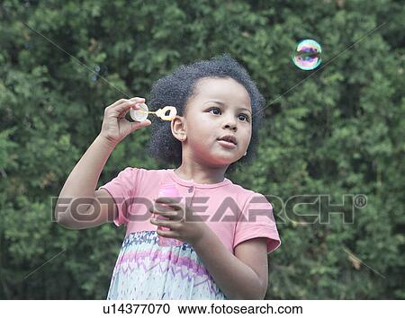 Stock Image - Girl blowing bubbles outdoors. Fotosearch