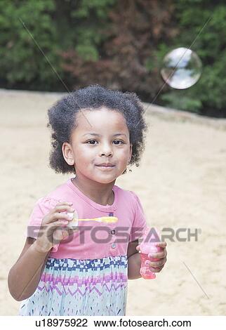 Stock Image - Girl blowing bubbles outdoors. Fotosearch